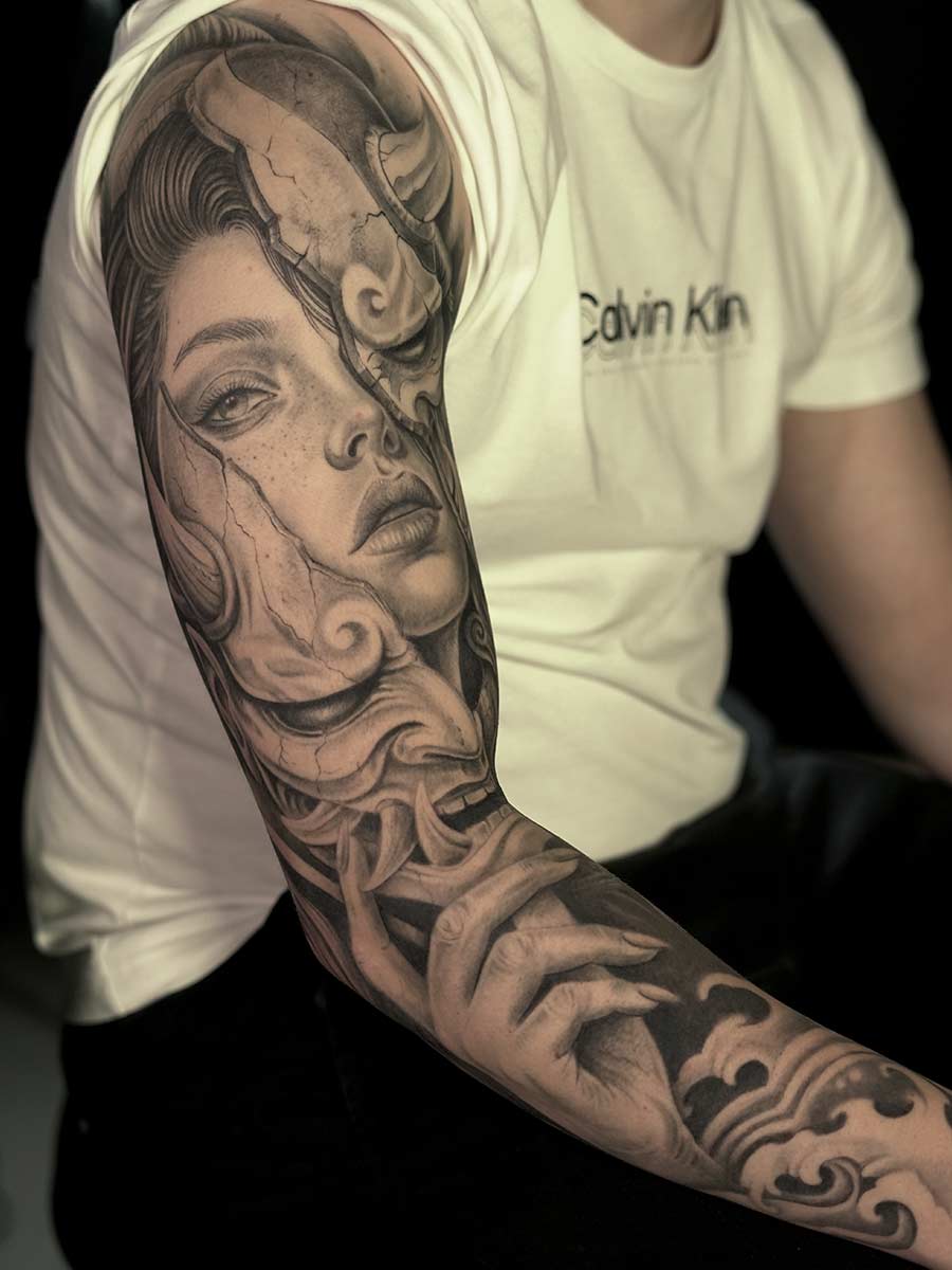 Black-and-grey Japanese-inspired full sleeve tattoo with portrait and waves